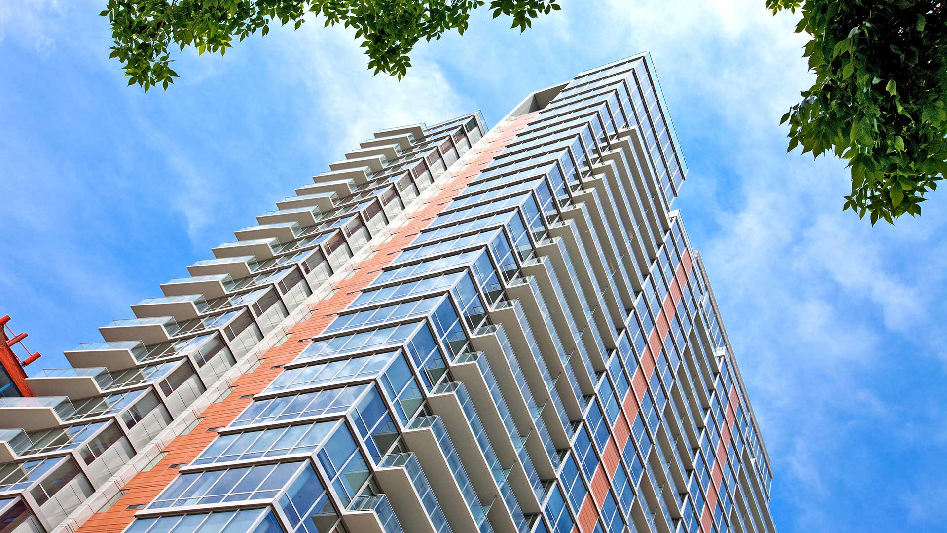 Looking up the Burnham Pointe apartment tower from the street below on a clear day. The building is mainly large glass windows and balconies all the way up.