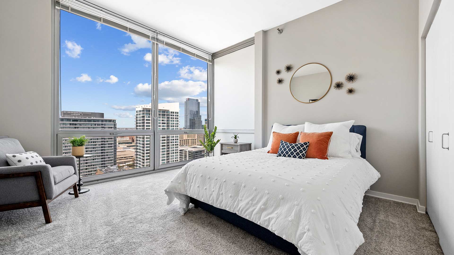 A bedroom in a residence at Burnham Pointe. A large bed is set on the right with floor-to-ceiling windows on the left showing the city outside.