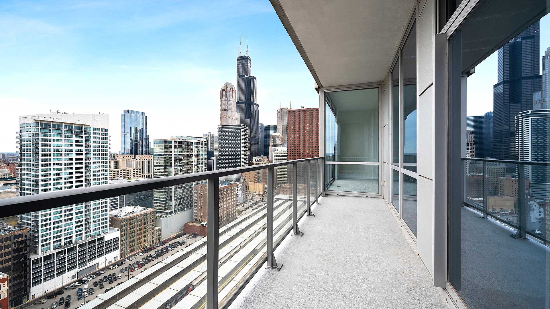 Looking down a private balcony in a residence at Burnham Pointe. The city is seen to the left with Willis Tower standing tall. Windows to the residence run along the right wall.